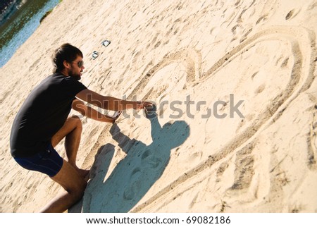 Young man drawing heart on the beach. Shoot on the nature.