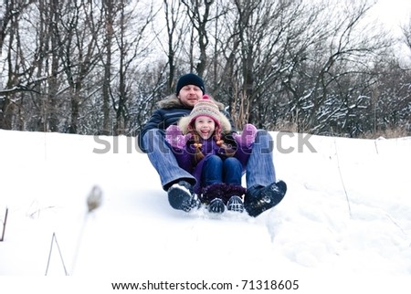 father and daughter riding on a sled in a winter woods