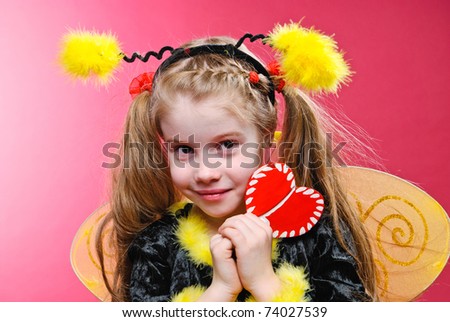 Pretty little girl dressed like a bee holding handmade heart. Studio shot.