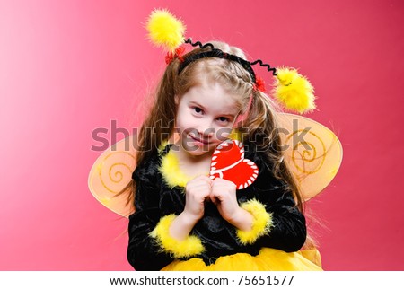Pretty little girl dressed like a bee holding handmade heart. Studio shot.