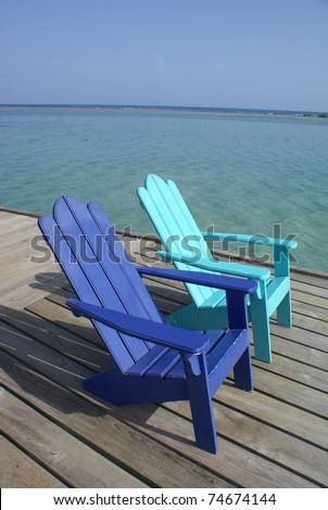 colorful adirondack chairs sit on a dock by the Caribbean sea
