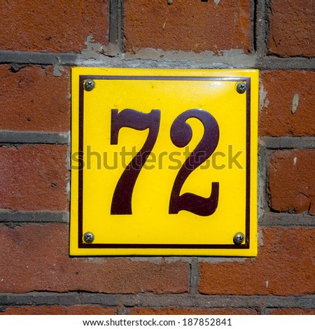 Enameled house number seventy two. Brown lettering on a yellow background.
