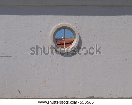 View on rooftops trough a round window in a white wall.