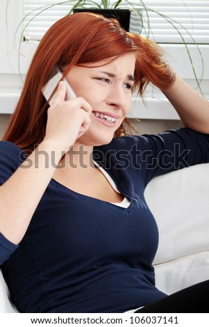 Upset and sad young woman sitting and talking by the phone. During phone conversation girl is crying.
