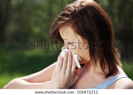 Young woman with allergy during sunny day is wiping her nose. Girl in summer dress with runny nose, having allergy and holding a tissue next to her face.
