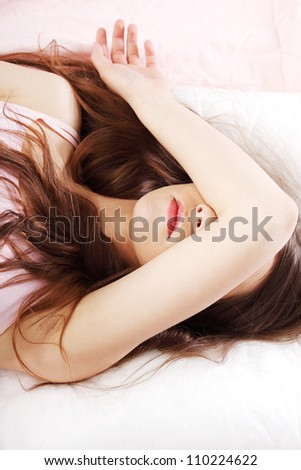 Sad woman is lying in bed with her arm on head and eyes. Young woman with long hair, wears pink underwear.