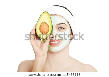 Young woman with a  smile holding avocado heaving face clay mask on the face in a spa