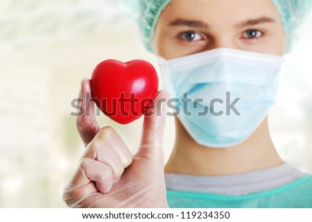 Male surgeon looking at camera at hospital and holding red heart, close up shot