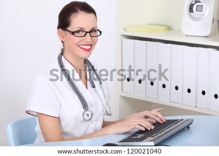 Happy female doctor in office working on pc computer