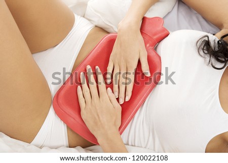 Close up of woman belly with hot water bottle in bed