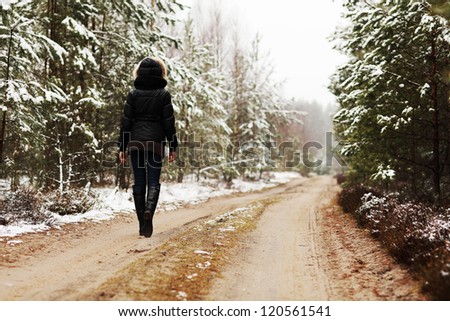 Woman is walking through forest in wintertime. Alone woman is going in cold day.