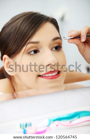 Young beautiful woman plucking her eyebrows with tweezers at her bathroom