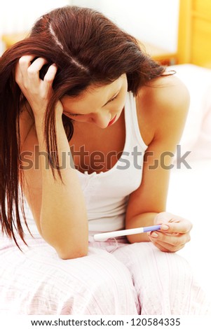 Beautiful young woman in the bedroom worrying because of the pregnancy test result.