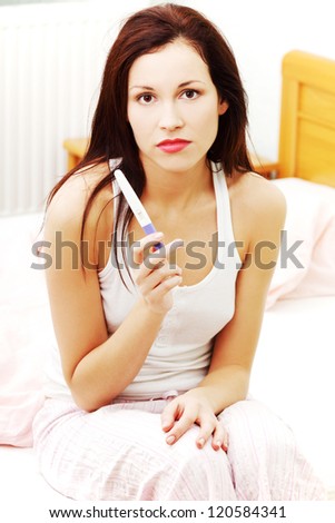 Beautiful young woman in the bedroom worrying because of the pregnancy test result.