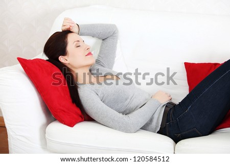Young beautiful woman lying on a couch, holding her hend on the forehead.