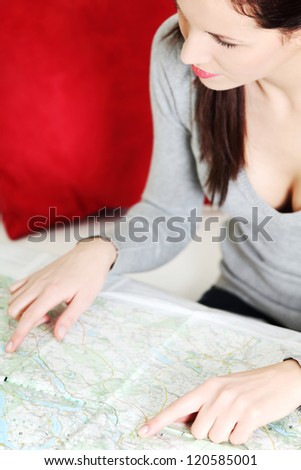 Young beautiful woman, sitting on a couch at home and having a look at a map.