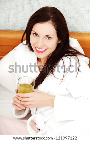 Beautiful relaxed woman dressed in a dressing-gown, drinking cold grean tea in the bed.