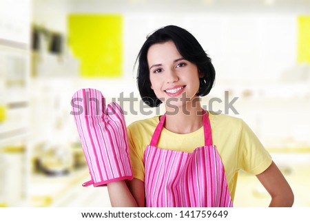 Young housewife in pink apron ang glove at kitchen