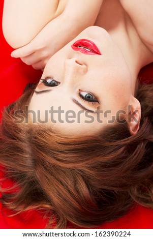 Attractive young naked woman lying on a red background. Red lipstick. Up front view. Close up. On red background.
