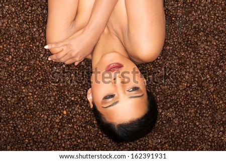 Attractive woman lying upside down on coffee seeds. Closeup.