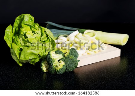 Lettuce,broccolli and leek lzing on cutting board. On black background.