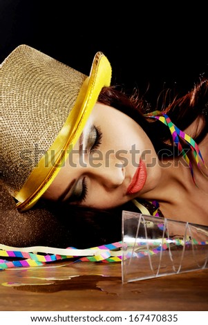 Young beautiful drunk woman sleeping on a table after celebrating new years eve. On black background.
