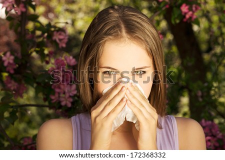 Young woman with allergy during sunny day is wiping her nose.