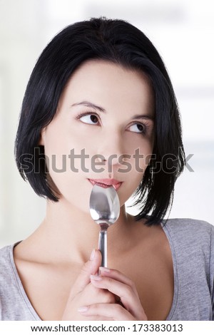 Portrait of young smiling woman with spoon in her mouth (pleasure from eating)