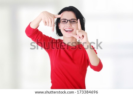 Smiling woman wearing red blouse is showing frame by hands. Happy girl with face in frame of palms.