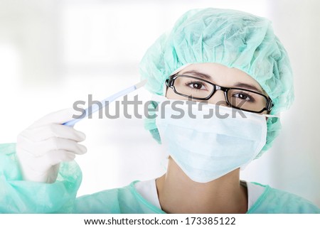 Portrait of woman doctor or nurse with surgical mask and cap holding scalpel