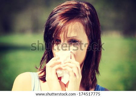 Young woman with allergy during sunny day is wiping her nose. Girl in summer dress with runny nose, having allergy and holding a tissue next to her face.