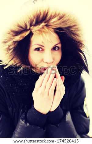 Beautiful woman trying to warm her hands with a breath in winter coat