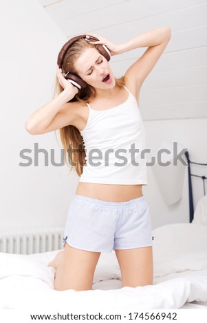 Beautiful caucasian woman in pajamas is listening to music on bed. Indoor background.
