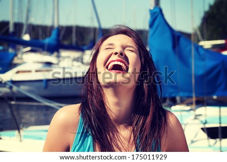 Happy Girl In Front Of Yacht Boat Is Laughing With Closed Eyes. Beautiful Young Woman With Dispelled Hair In Yacht Harbor.