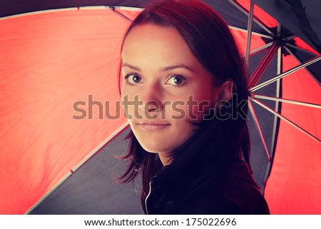 Beautiful teen woman dressed in black under red and black umbrella isolated on white background