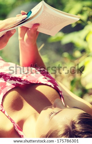 Reading woman laying in a park bench in summer.