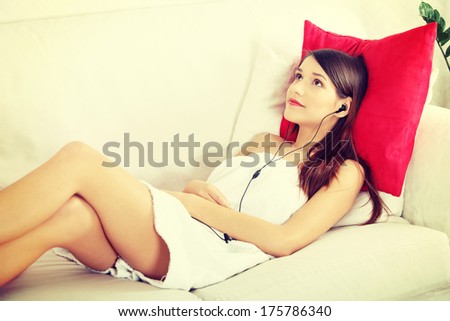 Listening to music. Young woman relaxing at home after bath, listening to music, lying on sofa in towel.