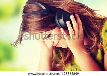 Beautiful teenage girl in a green dress listening to music with big headphones Beautiful teenage girl in a green dress listening to music with big headphones