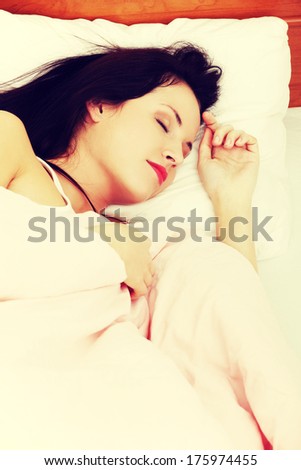 Site view closeup of a young beautiful woman sleeping in the bed, resting her left hand next to her face.