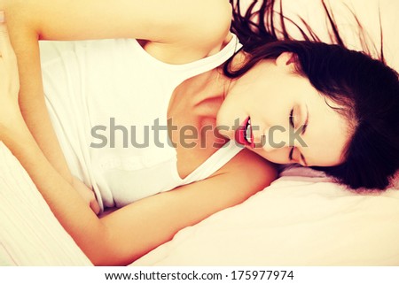 Closeup of a fit and shaped woman having a stomach ache, ambracing her belly in bed.