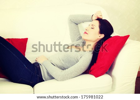 Site view portrait of a young beautiful smiling woman lying on a couch, holding her hend on the forehead.