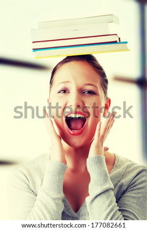 Young caucasian woman (student) with books on her head screaming with fear