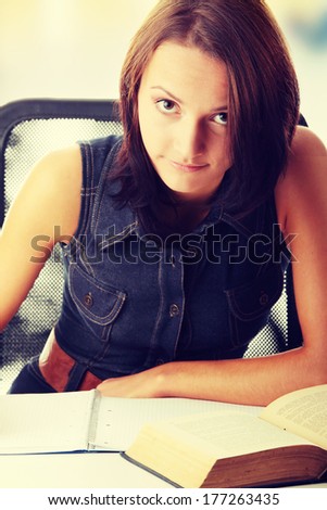 High school or college female student sitting by the desk, reading book and making notes in notepad.