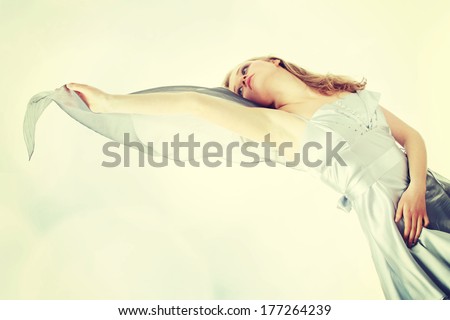 Young beautiful blond woman in elegant, evening, silver dress dancing with wind (hair blowing)