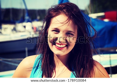 Beautiful young woman with dispelled hair in yacht harbor. Happy girl in front of yacht boat.