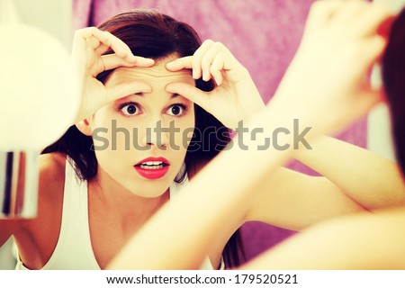 Mirror reflection of a woman worrying because of wrinkles on her forehead.