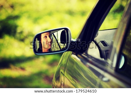 Face of women driving the car which is visible in mirror.