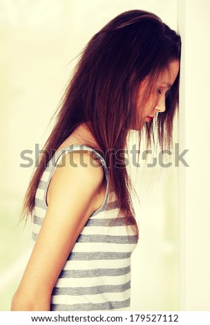 Site view of a young female teen being depressed, resting her head on a wall, on white.