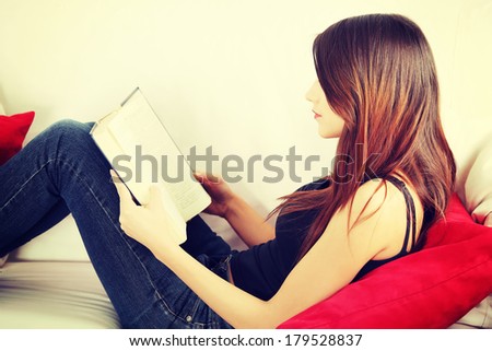 Beautiful woman reading a book, sitting on a sofa in a living-room