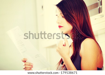 Stressed young caucasian woman in the kitchen drinking something hot and reading bill